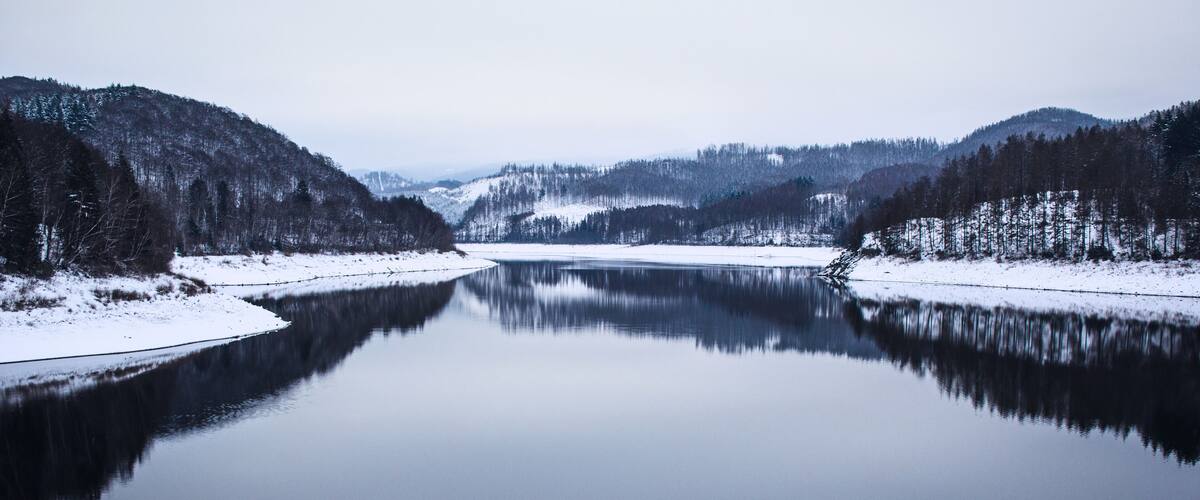 A calm river surrounded by snow-covered hills and dense forests.
