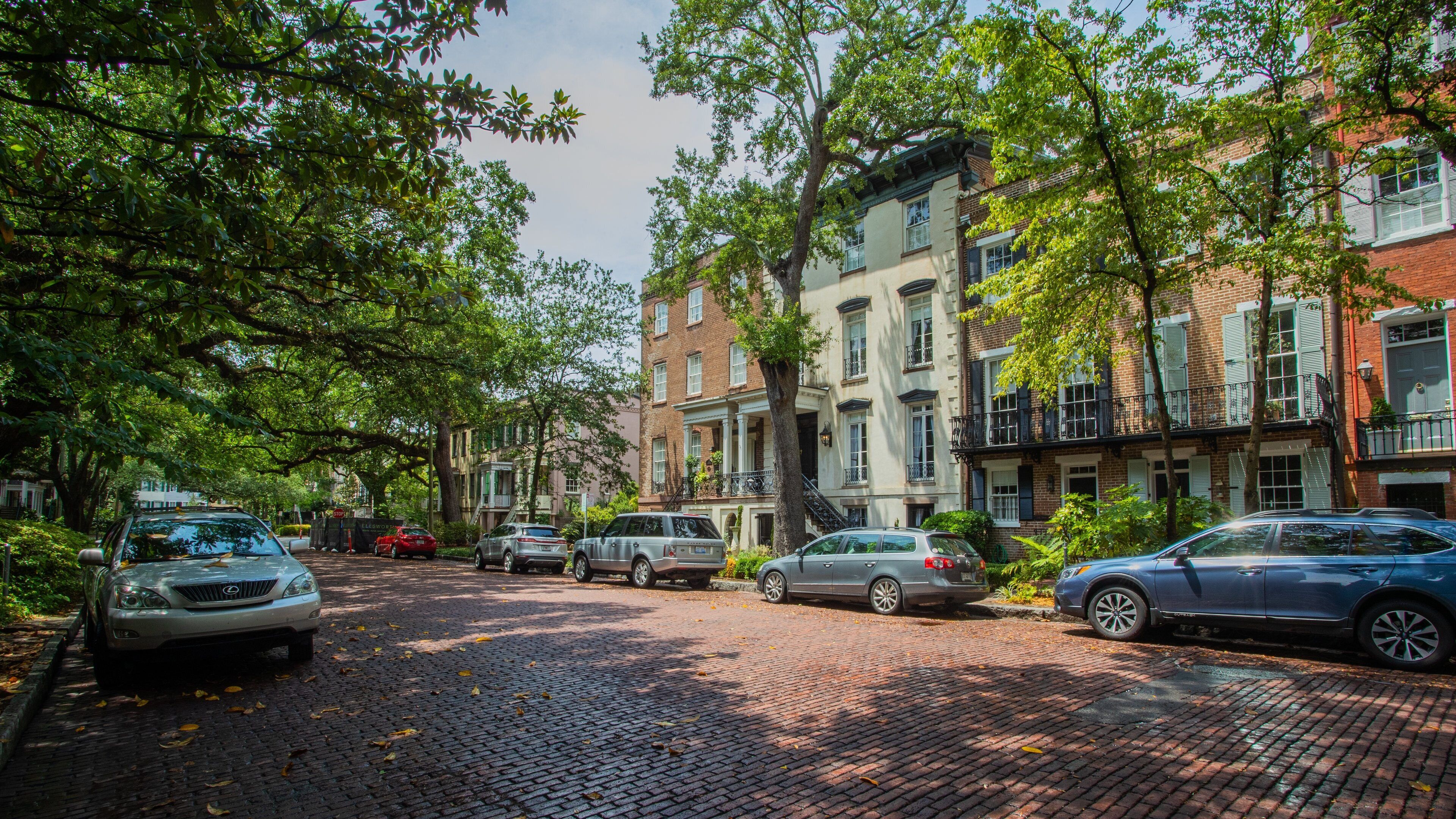 A cobblestone street lined with brick buildings and parked cars.