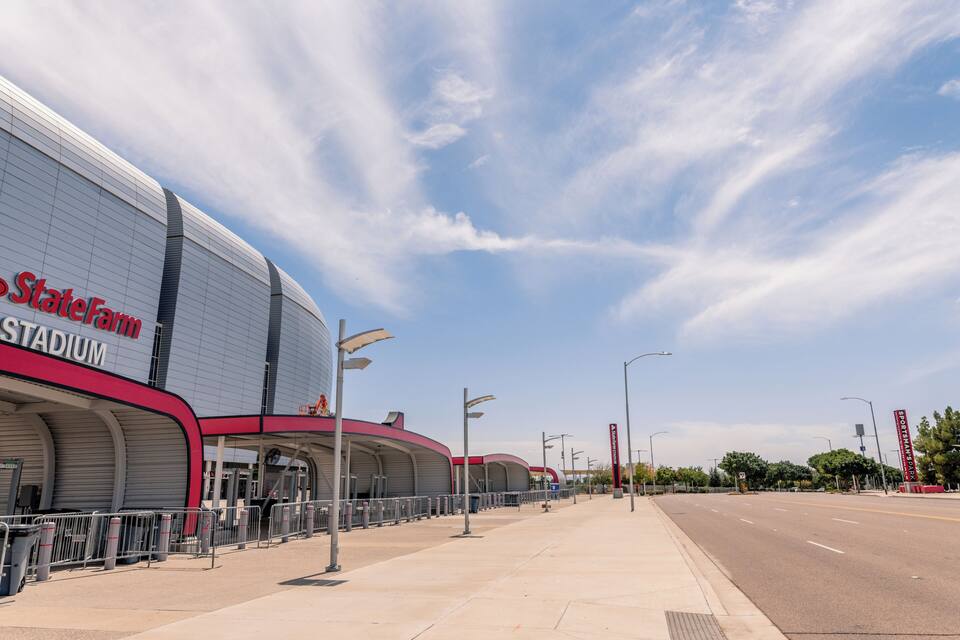 State Farm Stadium with a clear sky and a wide road in the foreground.