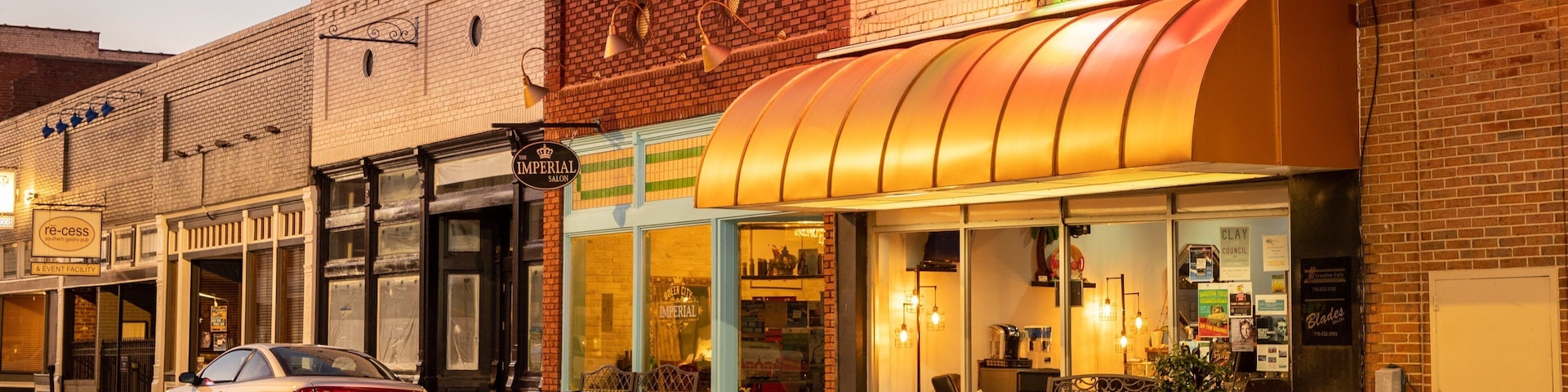 A street with a car parked on the side, a building with a neon sign, and a brick facade.