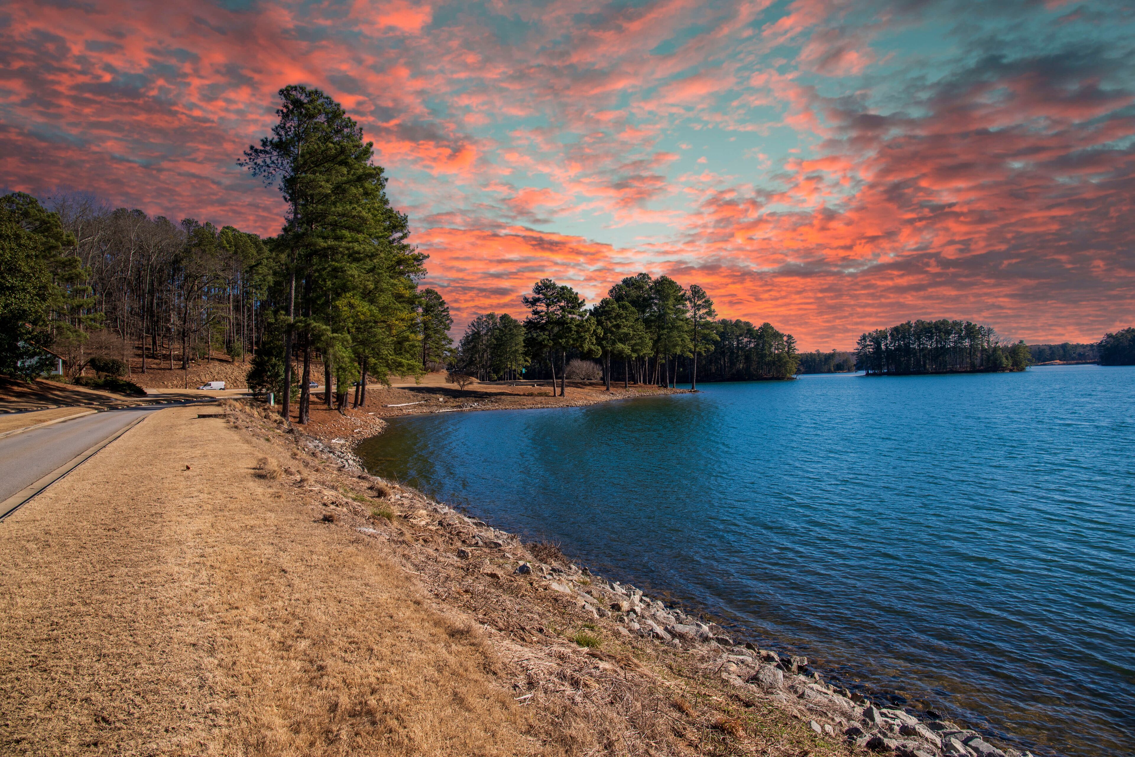 vast blue rippling water at Lake Lanier with the sun reflecting off the water and lush green trees with rocks along the banks and powerful clouds at sunset in Gainesville Georgia USA