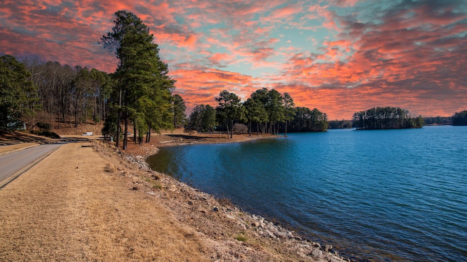 vast blue rippling water at Lake Lanier with the sun reflecting off the water and lush green trees with rocks along the banks and powerful clouds at sunset in Gainesville Georgia USA