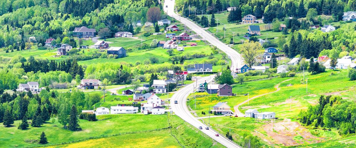 Les Eboulements, Charlevoix, Quebec, Canada cityscape or skyline with main highway steep curvy road going vertically up, patch farm green dandelion field, scattered village houses