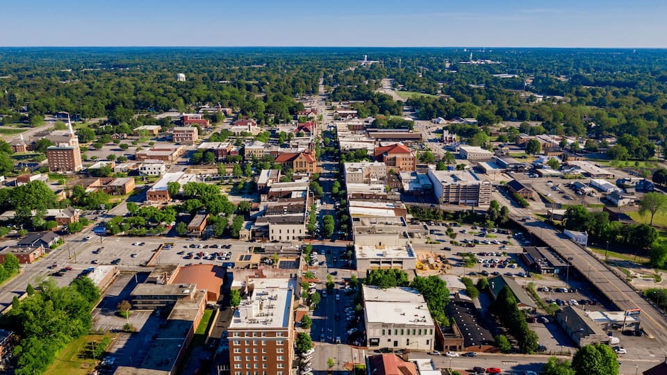 An aerial view of a city with a central road, surrounding buildings, and a distant water tower.