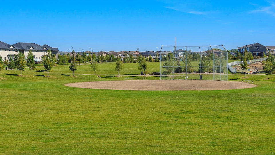A baseball field surrounded by residential houses and a modern building.