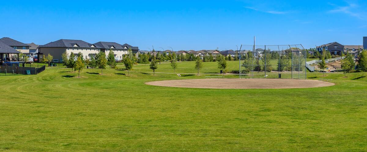 A baseball field surrounded by residential houses and a modern building.