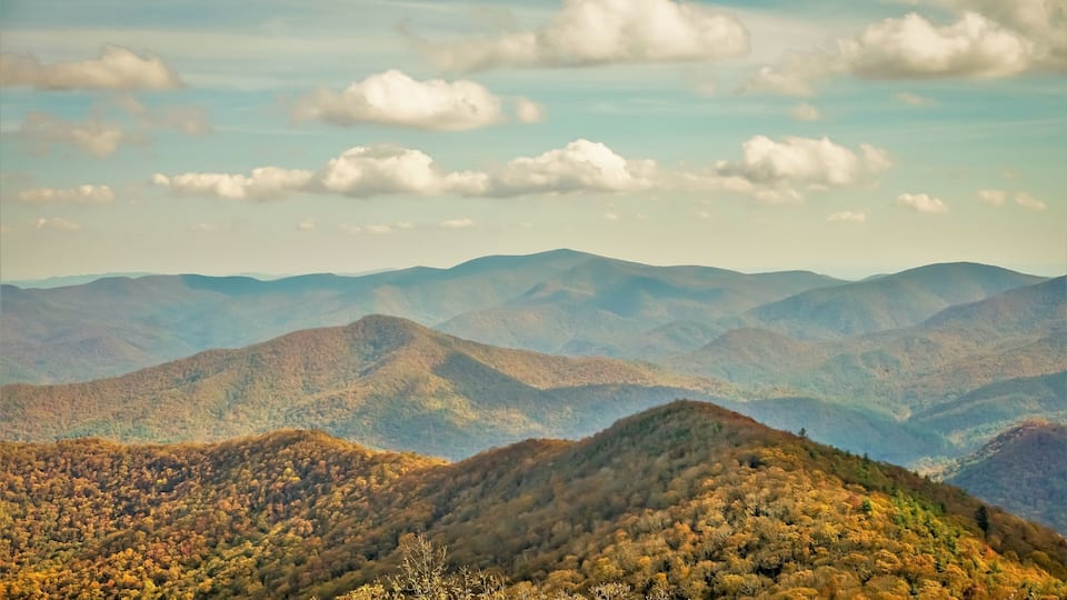 A mountainous landscape with autumn foliage and scattered clouds.