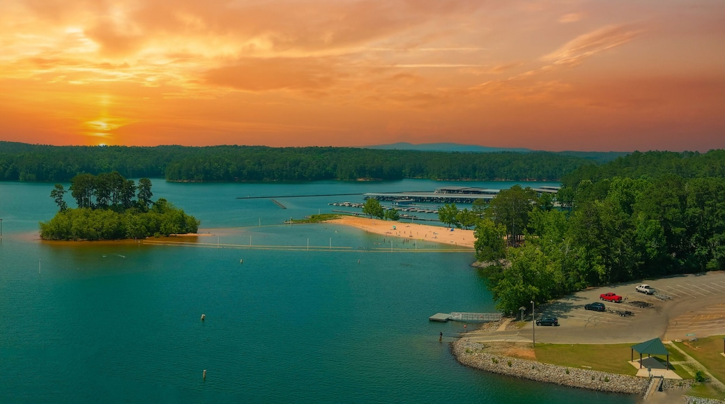 an aerial panoramic of the rippling blue waters of Lake Allatoona surrounded by lush green trees, grass and plants with powerful clouds at sunset at Victoria Beach in Acworth Georgia USA