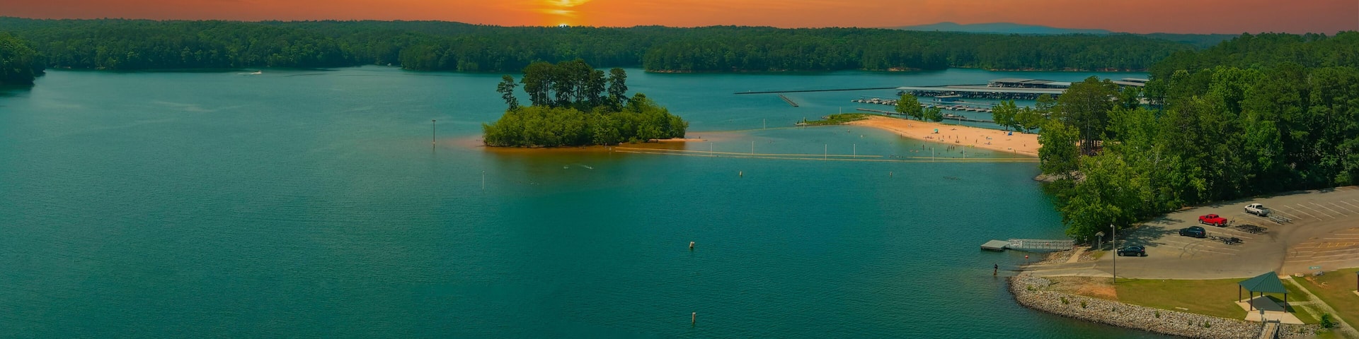 an aerial panoramic of the rippling blue waters of Lake Allatoona surrounded by lush green trees, grass and plants with powerful clouds at sunset at Victoria Beach in Acworth Georgia USA