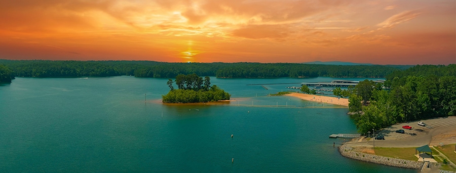 Un atardecer sobre un lago con una pequeña isla, un muelle y un aparcamiento.