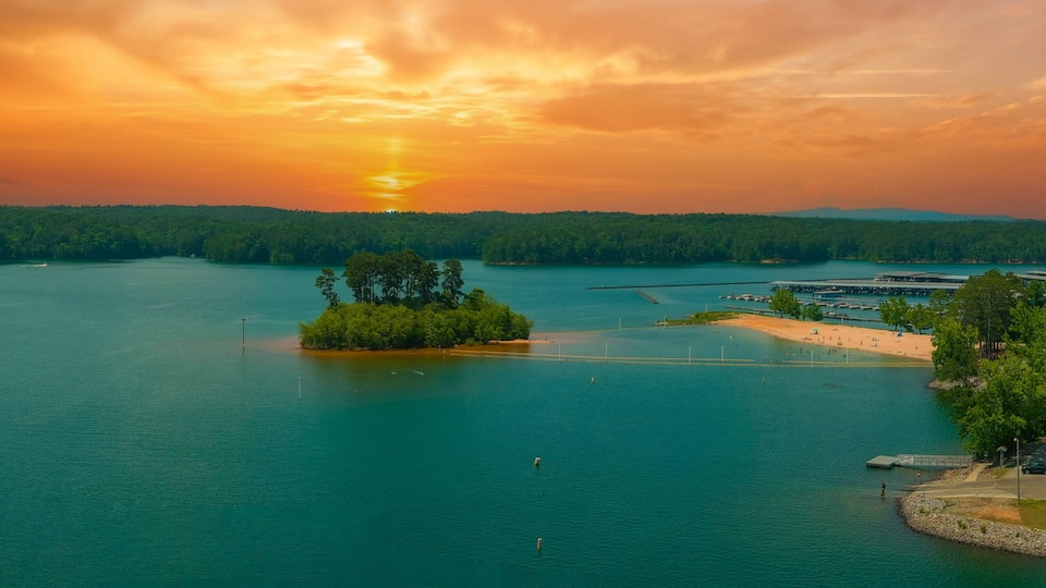A sunset over a lake with a small island, a dock, and a parking area.