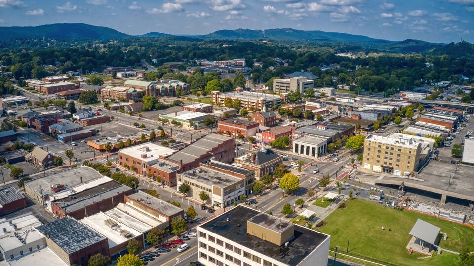 An aerial view of a town with a mix of historic and modern buildings, a central green space, and surrounding hills.