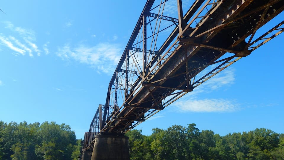 A steel bridge with a river below and trees in the background.