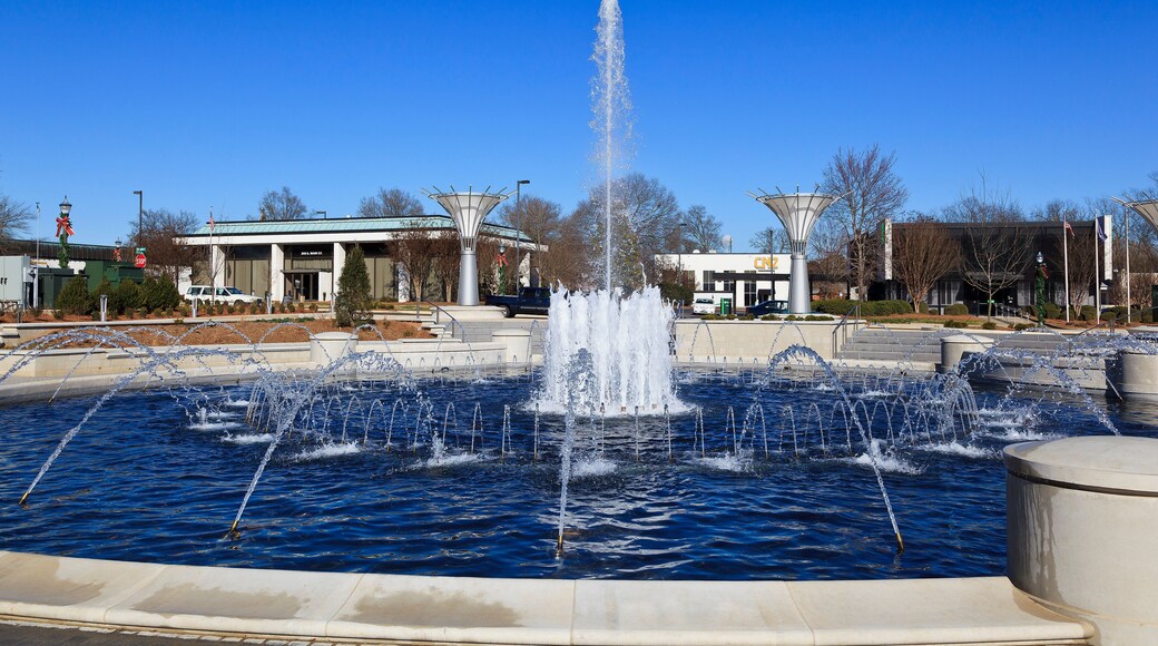 A fountain with multiple water jets in a public square, surrounded by buildings and trees.