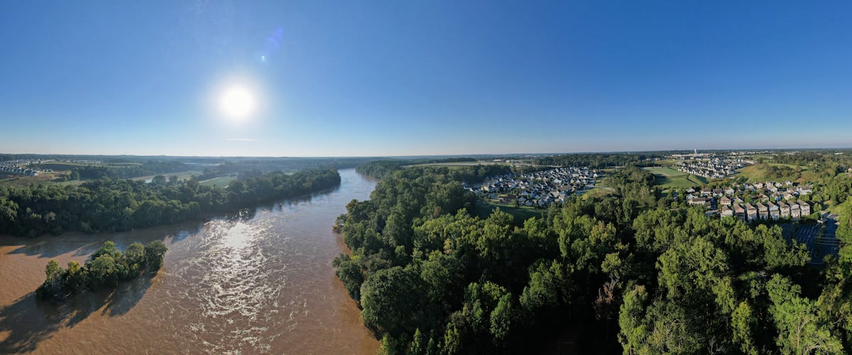 A river flowing through a densely forested area with a small town on the right bank.