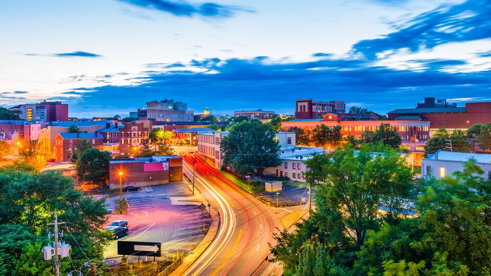 A cityscape at dusk with illuminated buildings and a curved road with light trails.