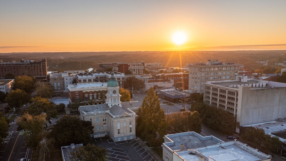 A cityscape at sunset with a prominent clock tower and a large building with a green dome.