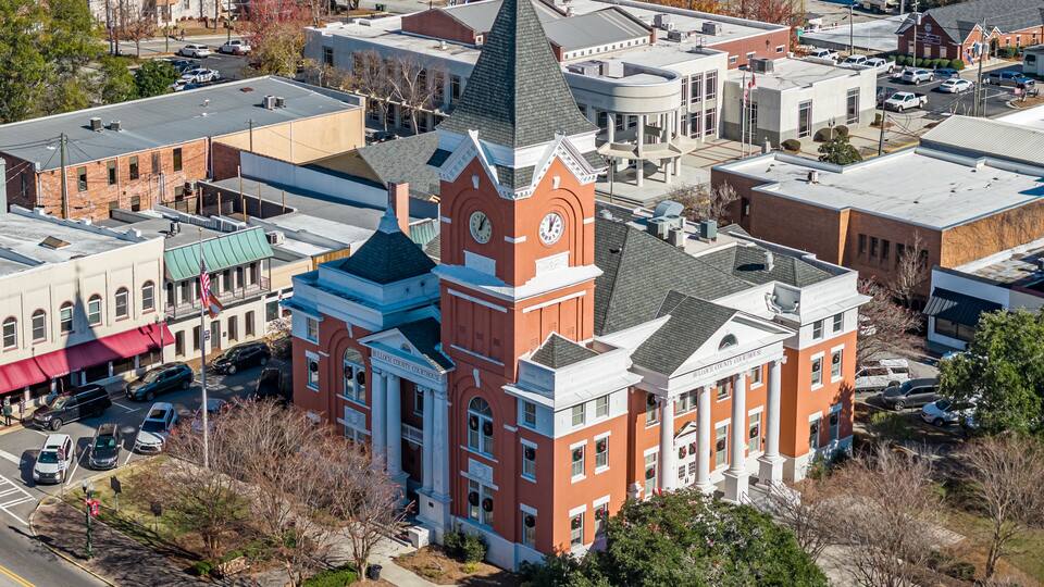 A courthouse with a clock tower, surrounded by other buildings and a parking lot.