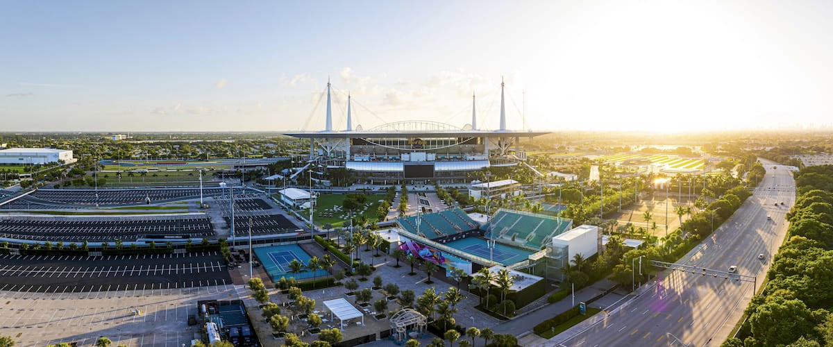 A stadium with a large seating area, a tennis court, and a parking lot.