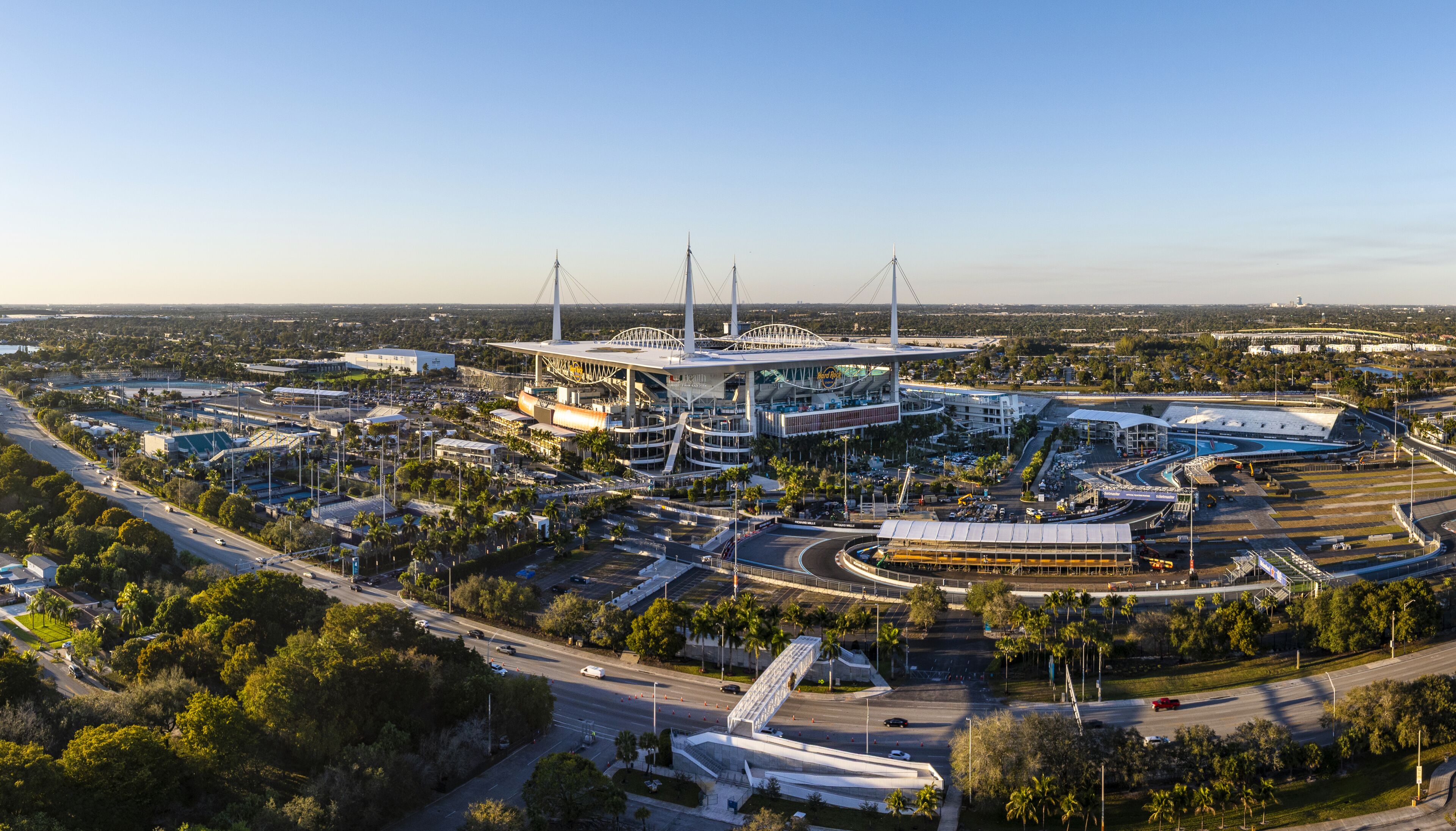 Miami Gardens, USA - 23 February 2026: Aerial view of Hard Rock Stadium, a modern coliseum bathed in the warm glow of the setting sun, surrounded by verdant trees and bustling roadways.