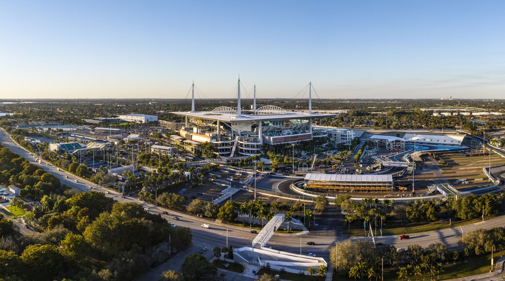 Miami Gardens, USA - 23 February 2026: Aerial view of Hard Rock Stadium, a modern coliseum bathed in the warm glow of the setting sun, surrounded by verdant trees and bustling roadways.