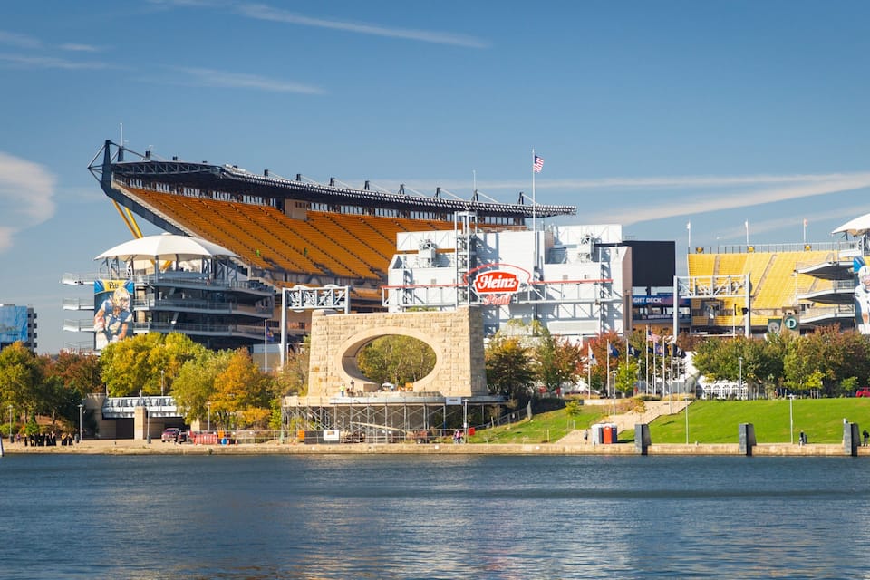 Un stade doté d’une structure de toit unique, d’un grand panneau publicitaire Heinz et d’une étendue d’eau au premier plan.