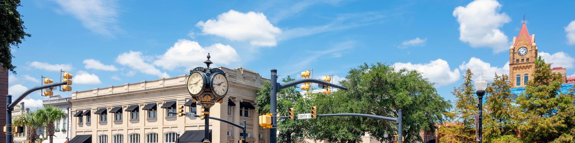 A historic downtown street with a prominent clock tower, a roundabout with directional arrows, and classic architecture.