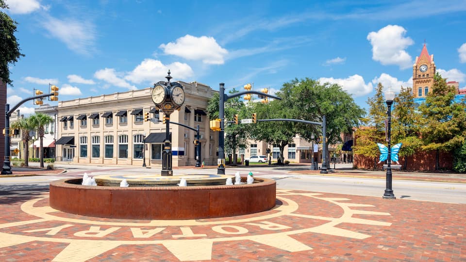 A historic downtown street with a prominent clock tower, a roundabout with directional arrows, and classic architecture.