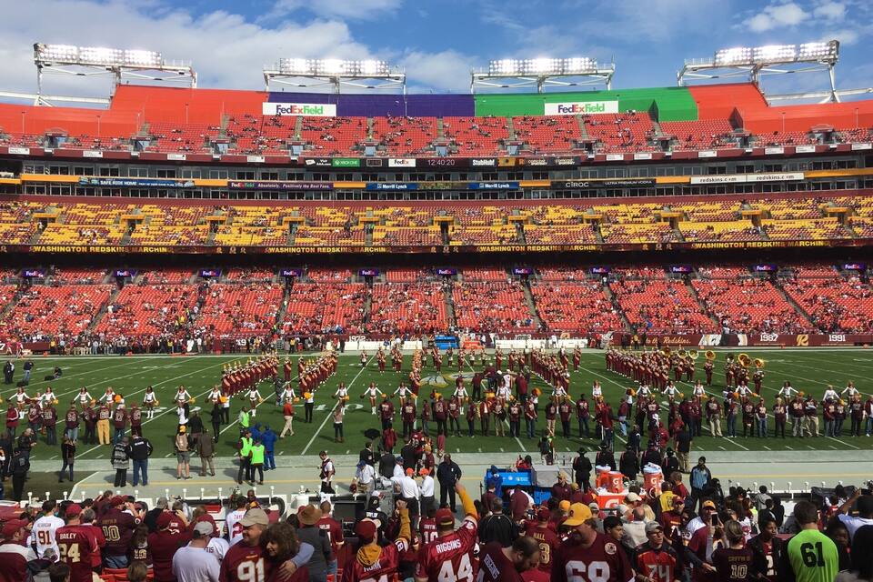 A stadium with red and yellow seats, a marching band, and a crowd of fans.