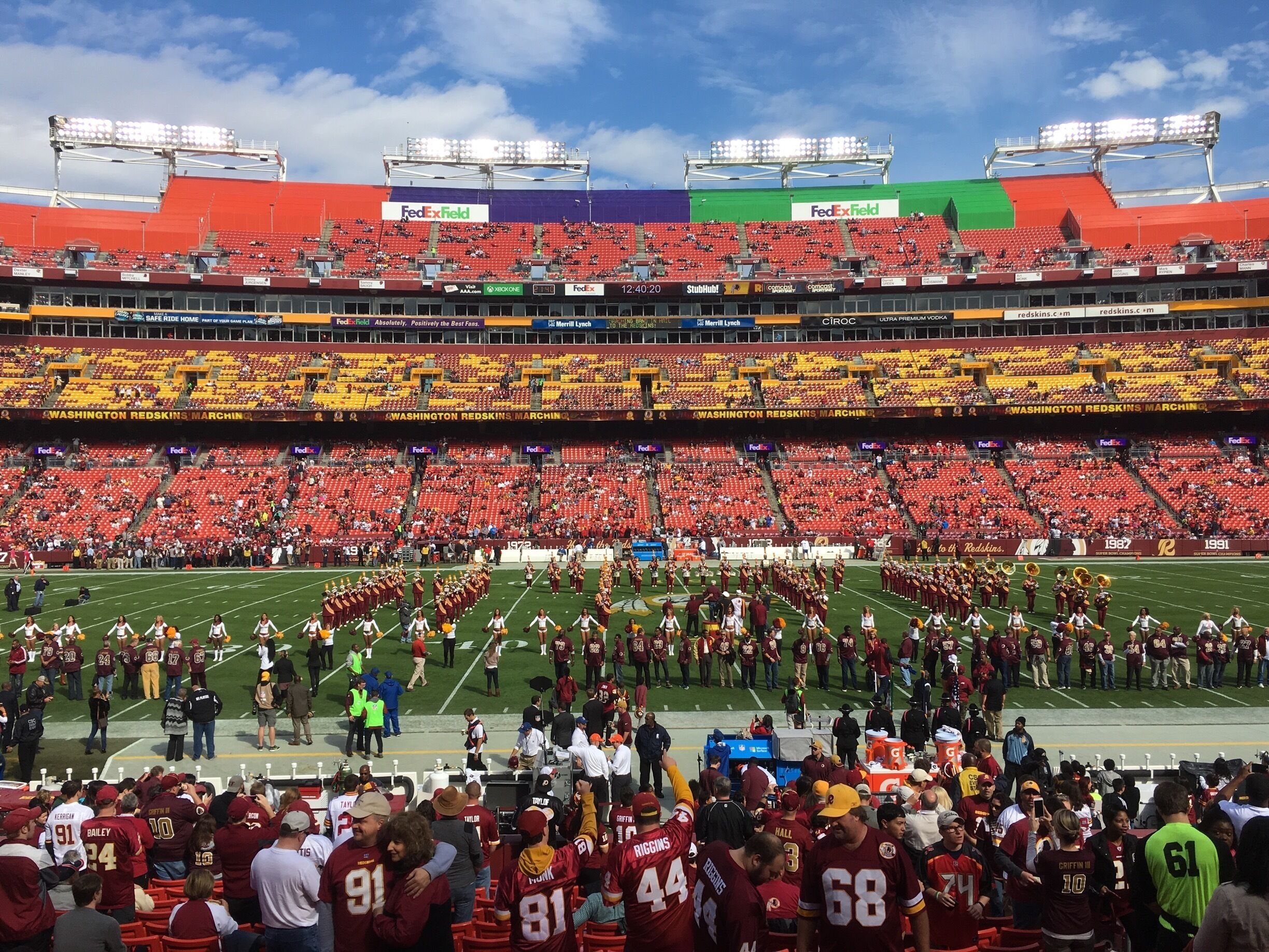 A stadium with red and yellow seats, a marching band, and a crowd of fans.