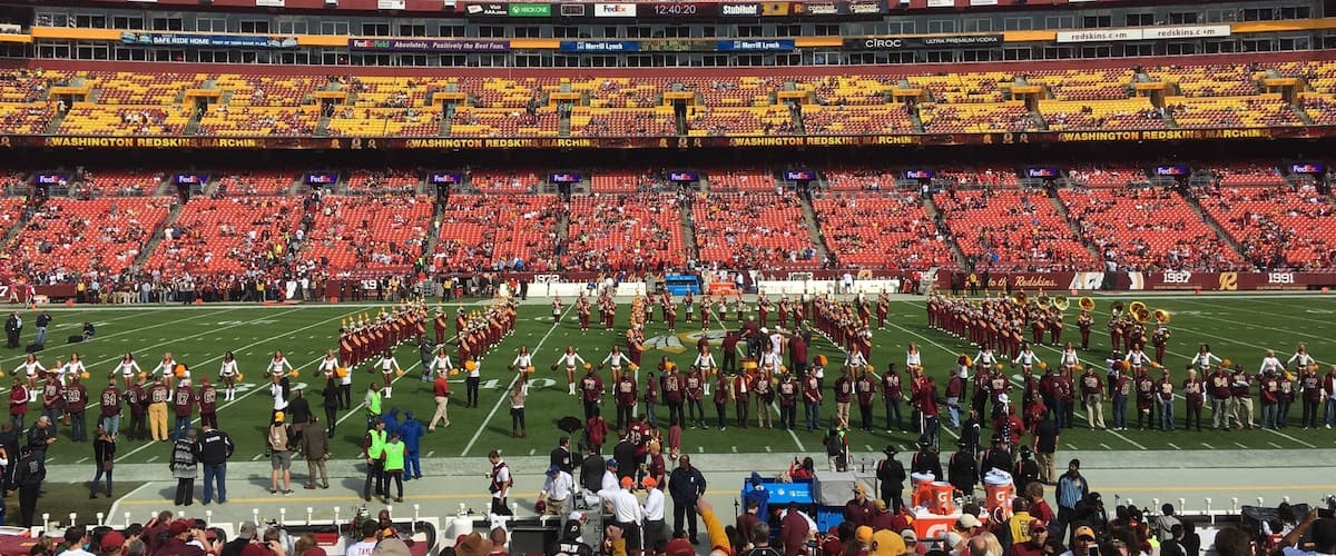 A stadium with red and yellow seats, a marching band, and a crowd of fans.