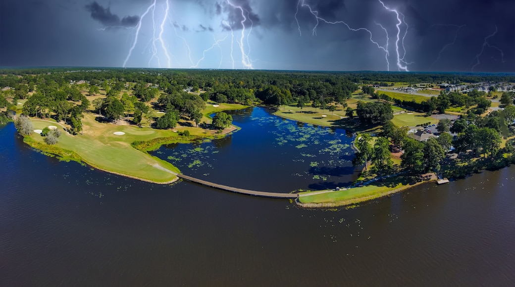 an aerial panoramic shot of a blue waters of Houston Lake surrounded by a golf course and lush green trees, grass and plants with powerful storm clouds and lightning in Perry Georgia USA