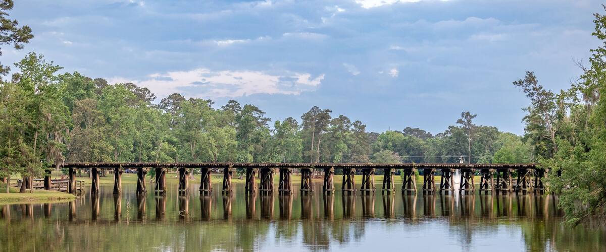 A wooden bridge over a calm lake with trees in the background.