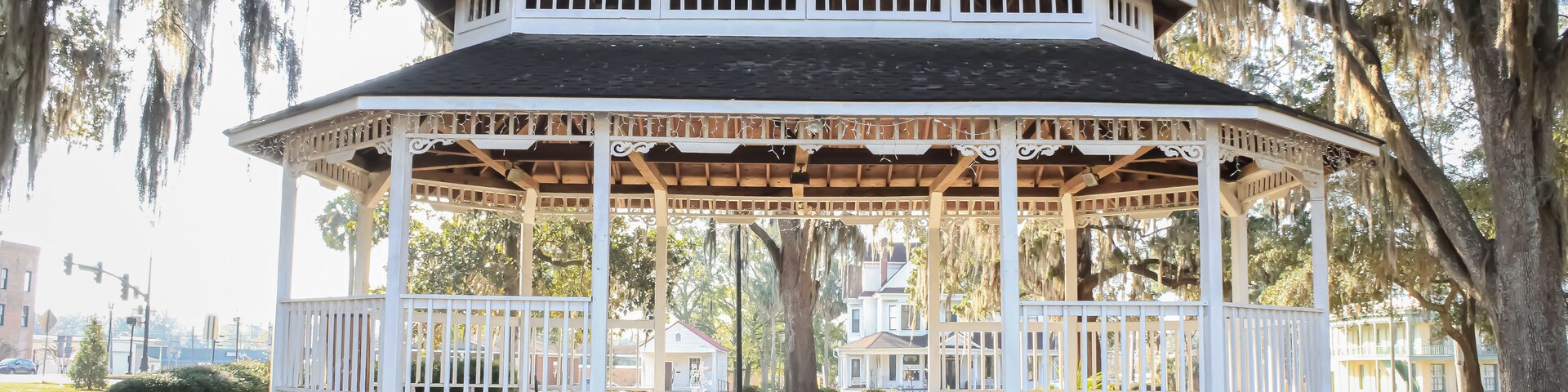 Um gazebo branco com varanda coberta, cercado por árvores com barba-de-espelho.