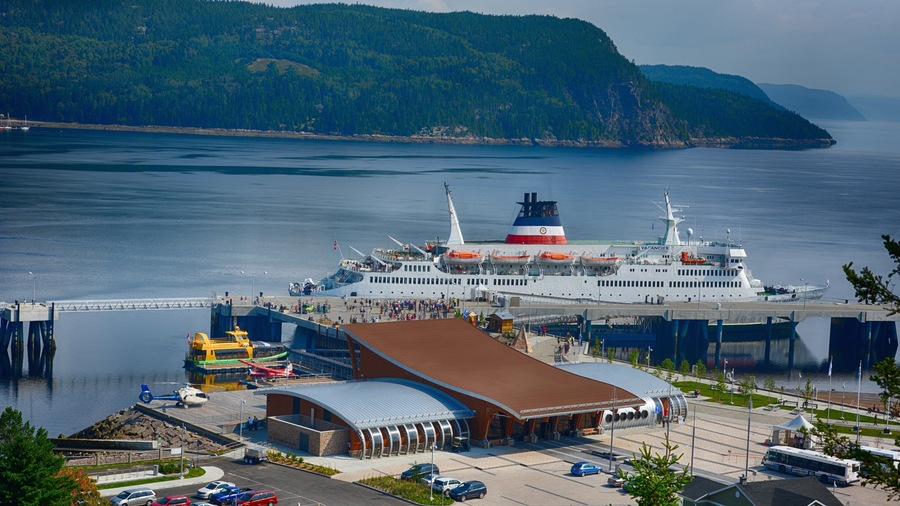 A ferry terminal with a large ferry docked, surrounded by a forested landscape and a bridge.