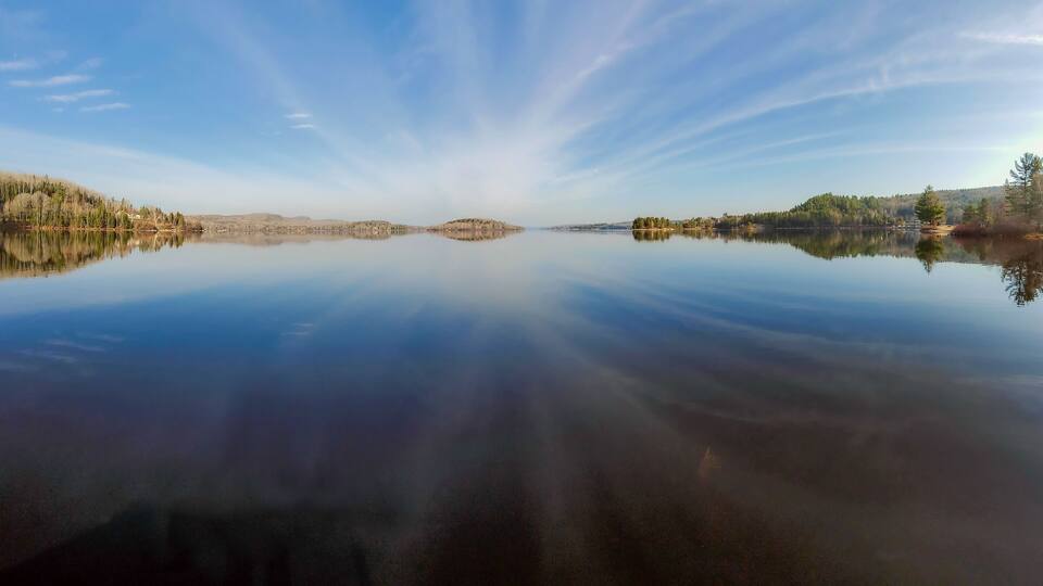 A calm lake with reflections of trees and a clear sky.