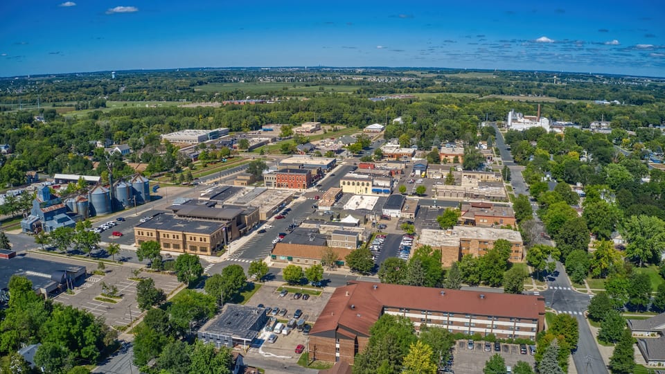 An aerial view of a town with a mix of industrial and residential buildings, surrounded by greenery and a clear blue sky.