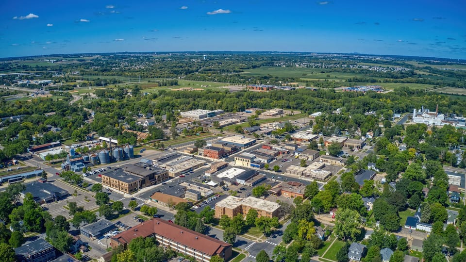 An aerial view of a town with industrial buildings, a large water tower, and surrounding green fields.