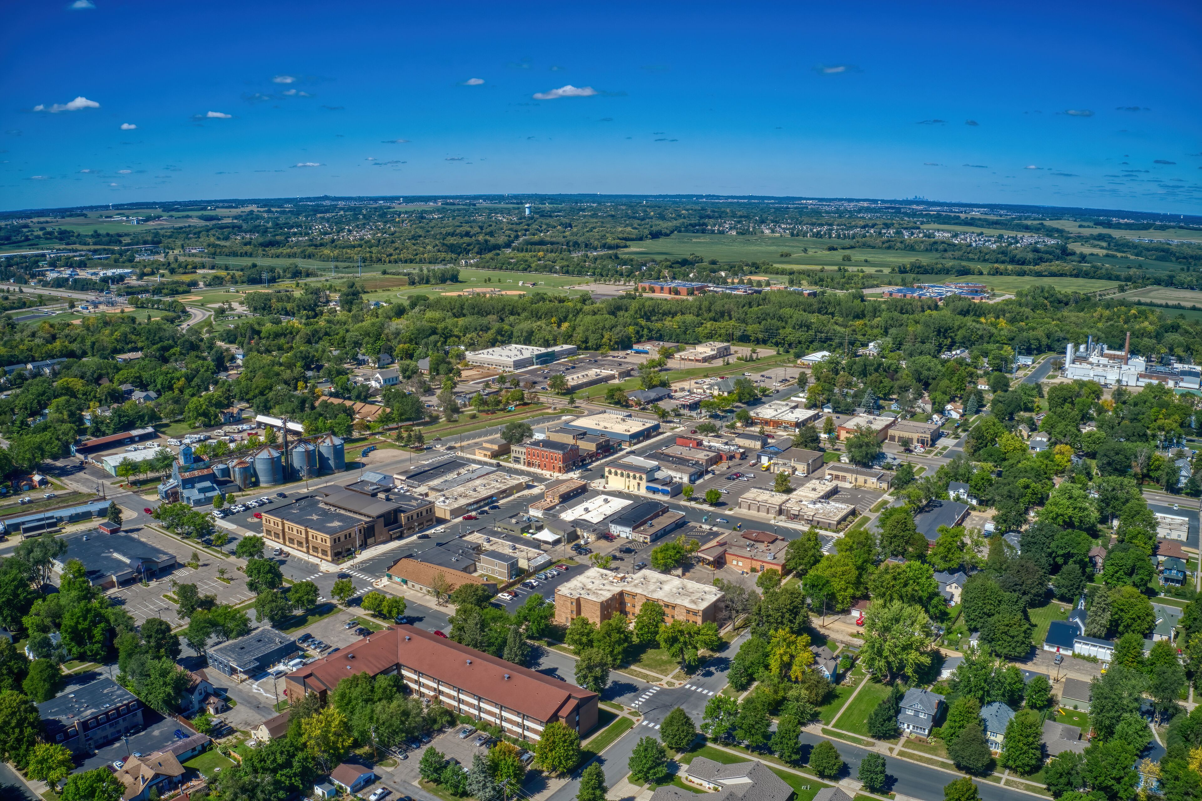 An aerial view of a town with industrial buildings, a large water tower, and surrounding green fields.