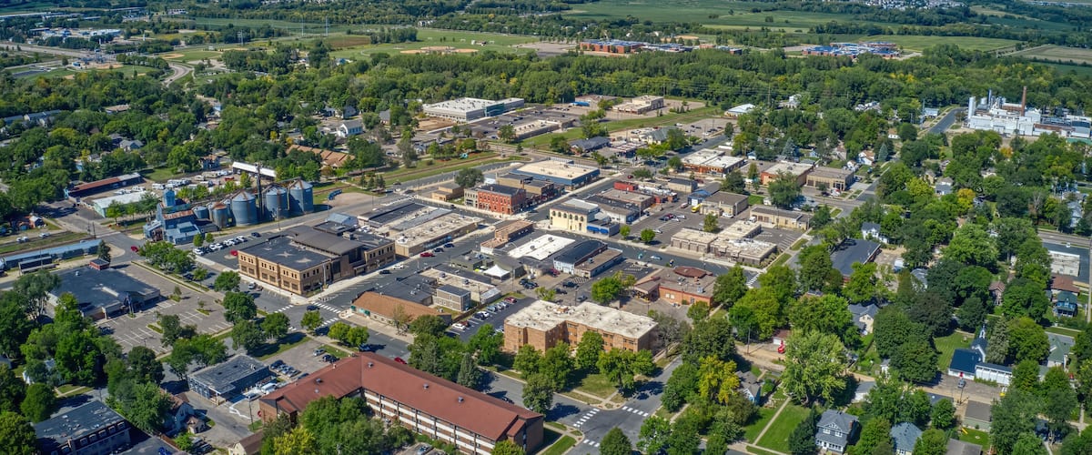 An aerial view of a town with industrial buildings, a large water tower, and surrounding green fields.