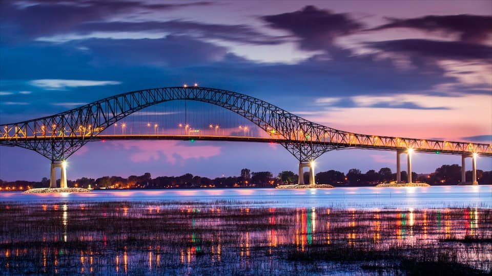 A large bridge spanning a body of water at twilight with city lights reflecting on the surface.