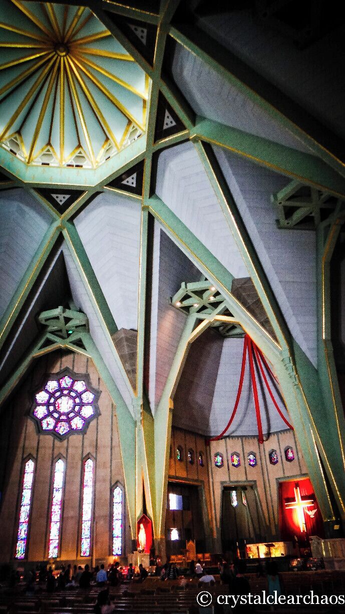 A church interior with a large stained glass window, geometric ceiling design, and a red cross.