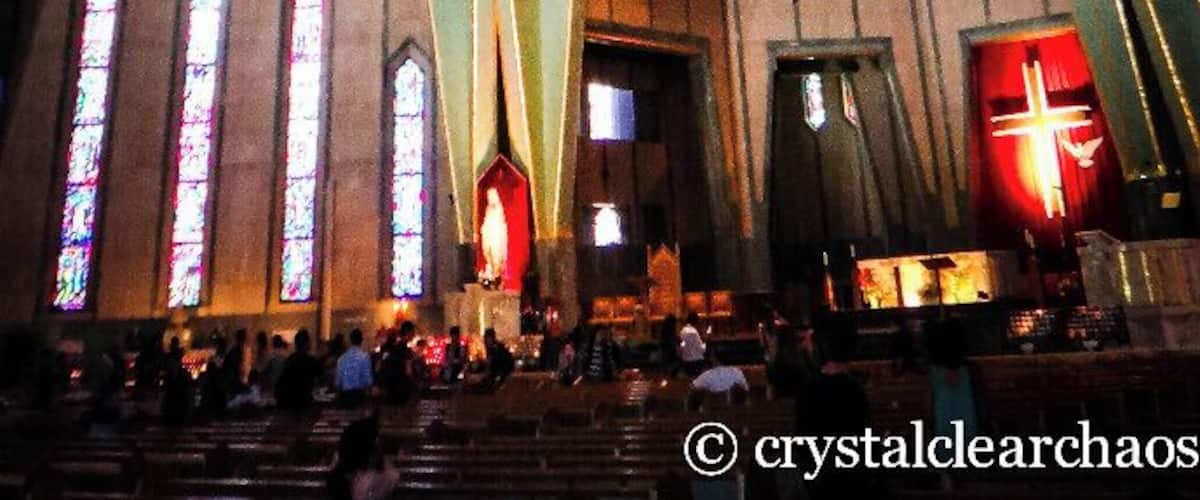 A church interior with a large stained glass window, geometric ceiling design, and a red cross.