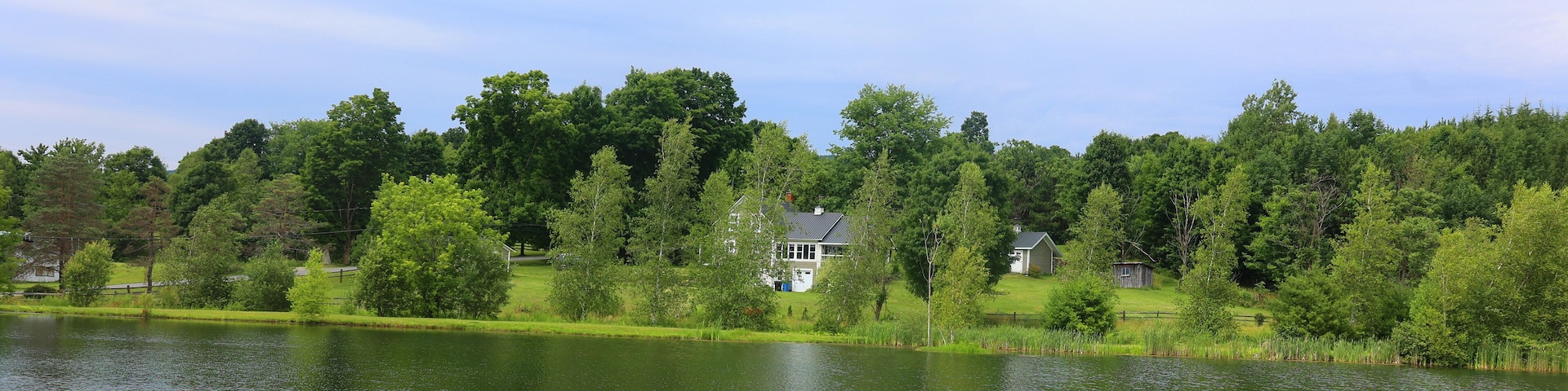 A lake with a house surrounded by trees and a grassy area.
