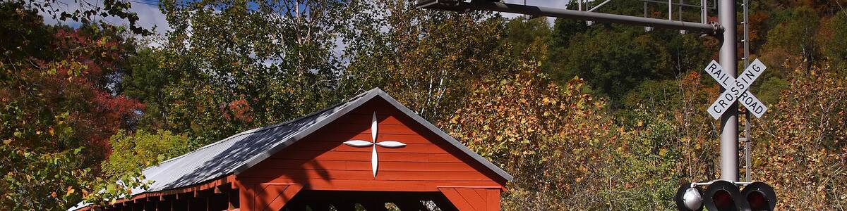 A red covered bridge, a railroad crossing signal, and a forested backdrop.