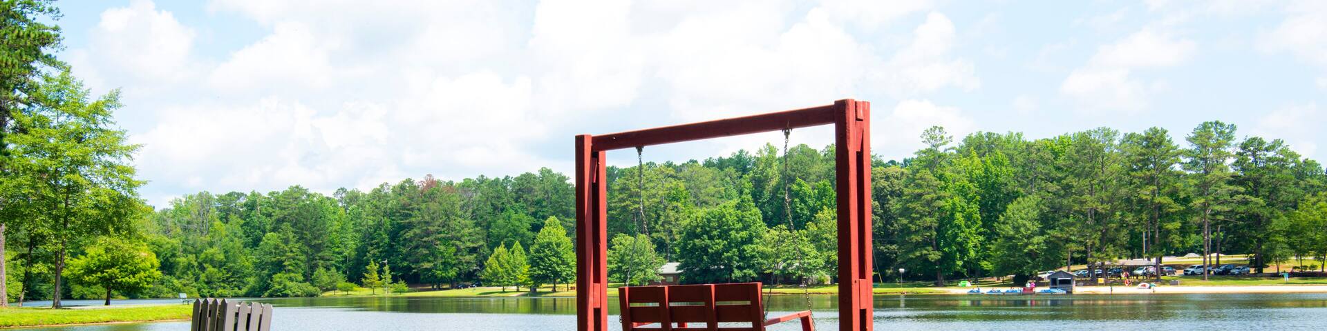 A park with a swing set, a lake, and a forest in the background.