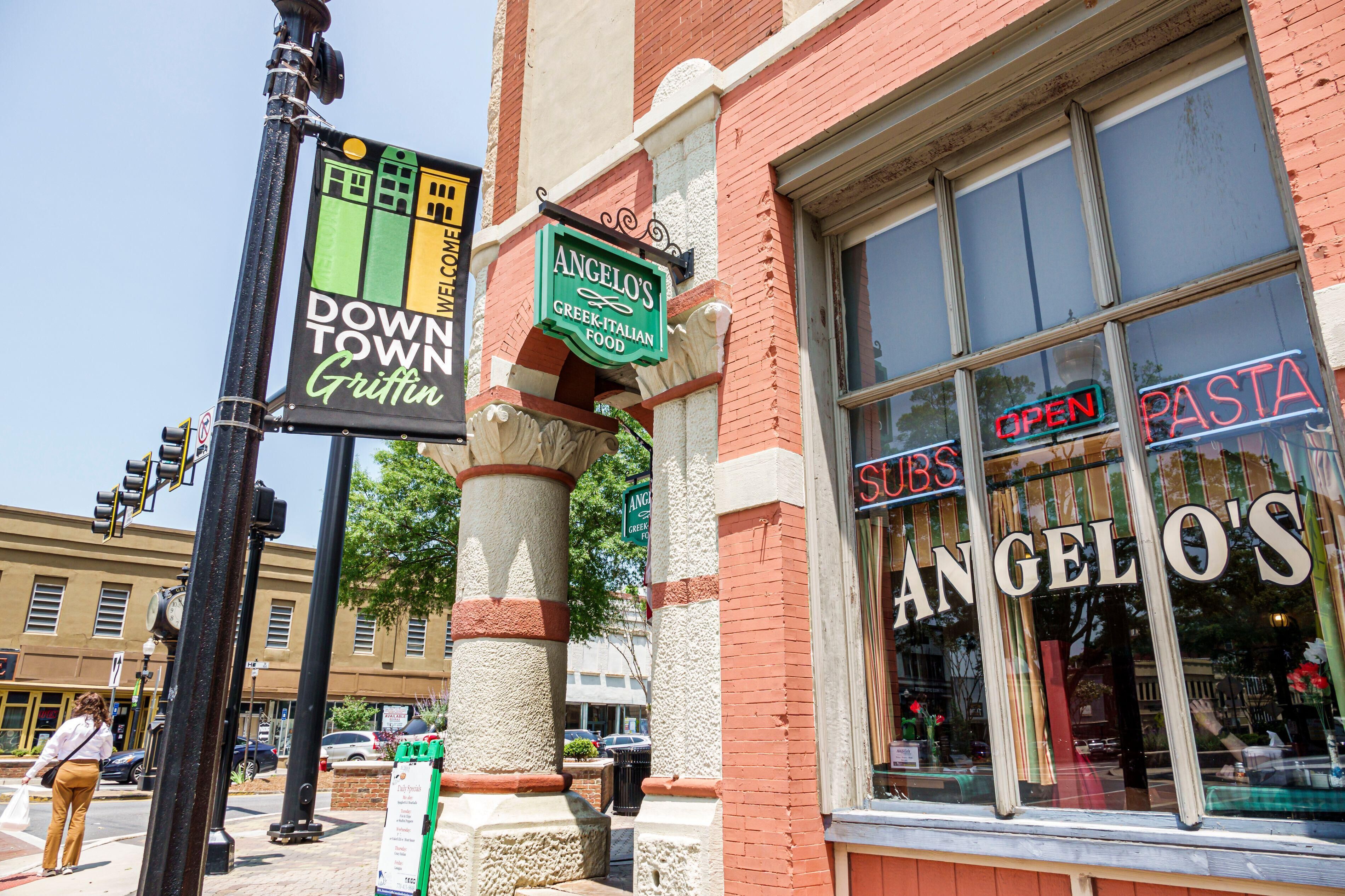 A street corner with a sign for Angelo's Greek-Italian food, a 'Downtown Griffin' sign, and a 'Pasta Subs' sign.
