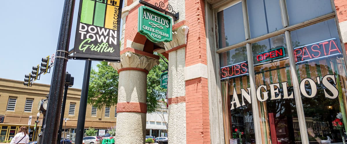 A street corner with a sign for Angelo's Greek-Italian food, a 'Downtown Griffin' sign, and a 'Pasta Subs' sign.
