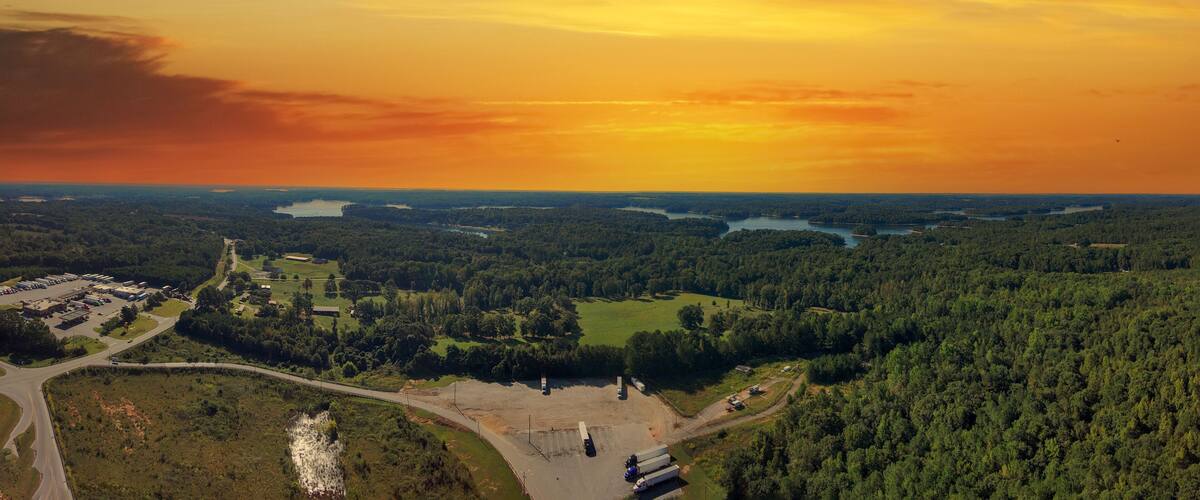 A forested landscape with a road, a parking lot, and a body of water.