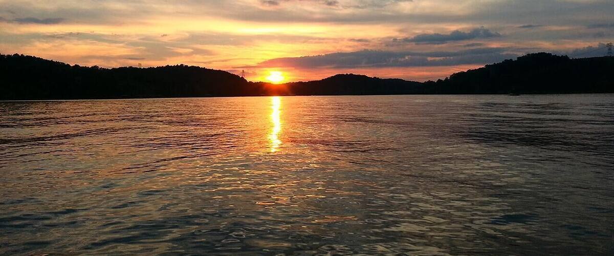 Un coucher de soleil sur un lac paisible, avec en arrière-plan la silhouette de collines.